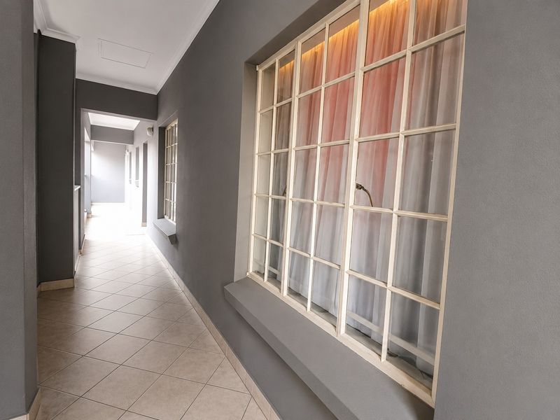 A well-maintained apartment hallway featuring neutral grey walls, tiled flooring, and large grid-pattern windows that allow for natural light.