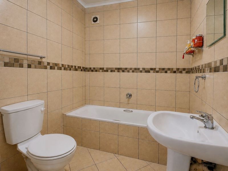 A functional bathroom featuring a bathtub, pedestal basin, and toilet, finished with neutral wall and floor tiling.