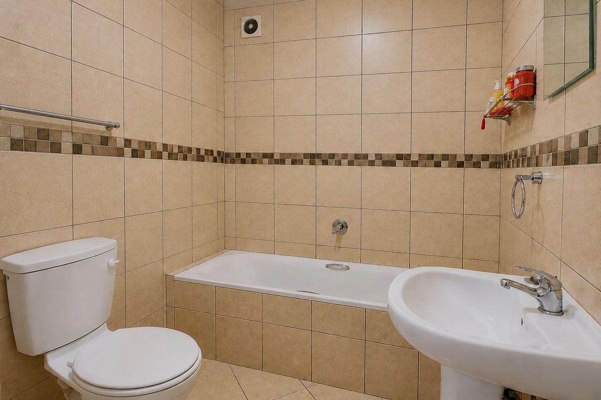 A functional bathroom featuring a bathtub, pedestal basin, and toilet, finished with neutral wall and floor tiling.