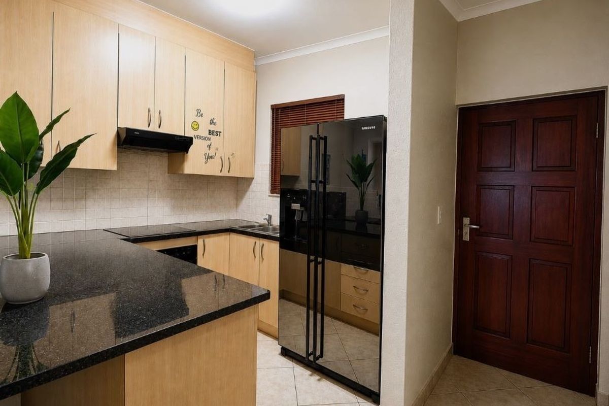 A functional kitchen featuring light wood laminate cabinetry, dark granite countertops, tiled backsplash, and ceramic flooring, with a dedicated space for a large refrigerator.