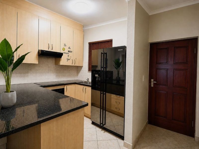 A functional kitchen featuring light wood laminate cabinetry, dark granite countertops, tiled backsplash, and ceramic flooring, with a dedicated space for a large refrigerator.
