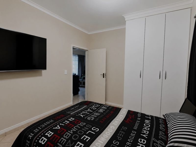 A well-maintained bedroom featuring neutral walls, tiled flooring, coving, and a large white built-in wardrobe with ample storage space.