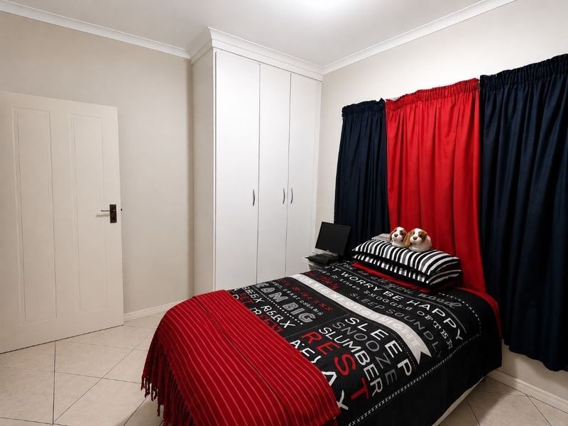 A well-maintained bedroom featuring neutral tiled flooring, white built-in cupboards, and classic cornice detailing, offering a clean and functional living space.