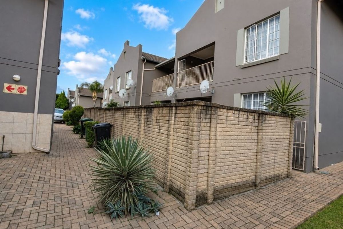 Exterior view of the apartment complex featuring a paved driveway, brick boundary wall, and upper-level balconies with satellite dish installations.
