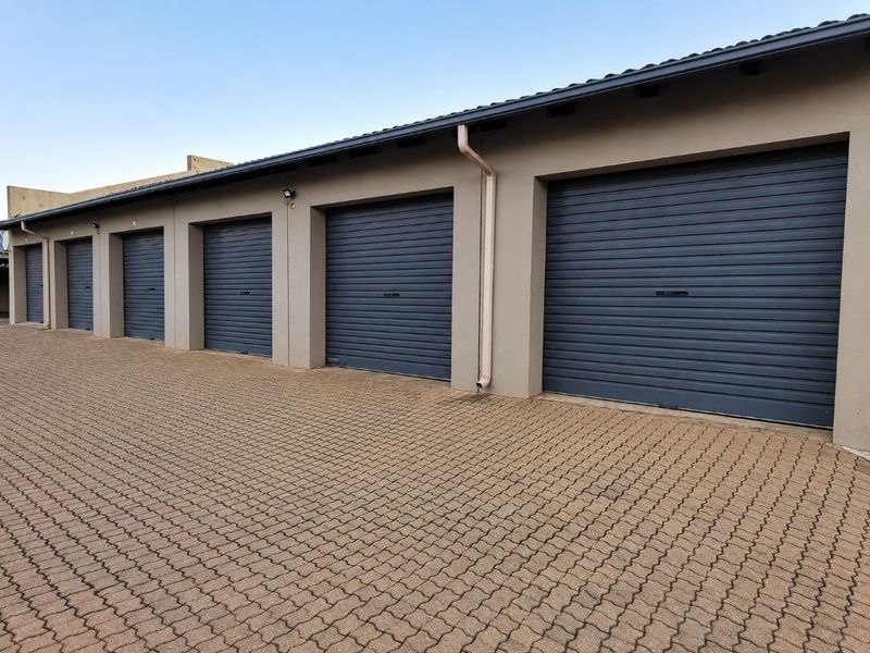 A row of modern garages featuring dark grey roller shutter doors and a neatly paved driveway area.