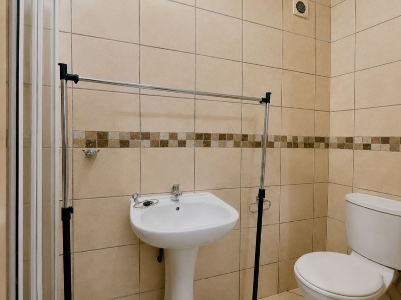A functional bathroom featuring tiled walls, a pedestal basin, a toilet, and a shower enclosure with an integrated extractor fan.