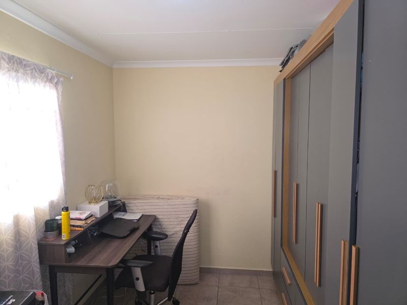 A bedroom featuring built-in cupboards with modern grey doors and wood-look trim, complemented by tiled flooring and neutral wall finishes.