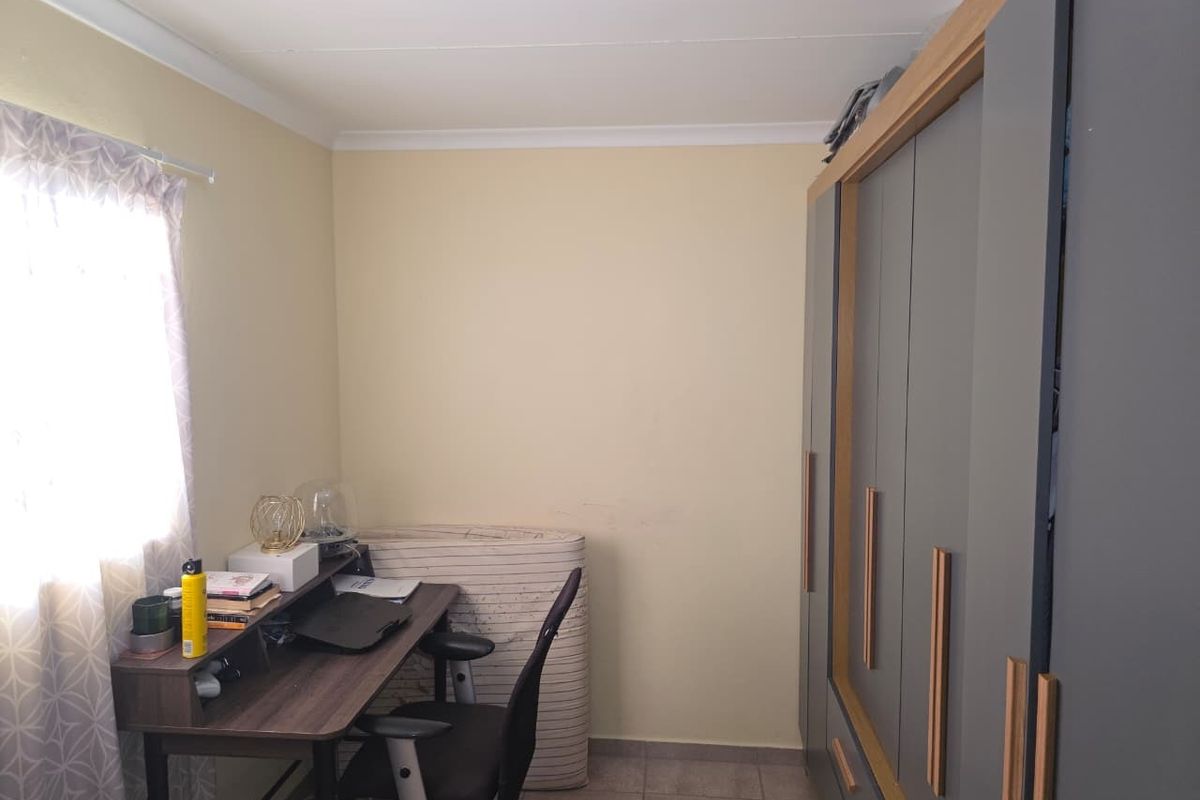 A bedroom featuring built-in cupboards with modern grey doors and wood-look trim, complemented by tiled flooring and neutral wall finishes.