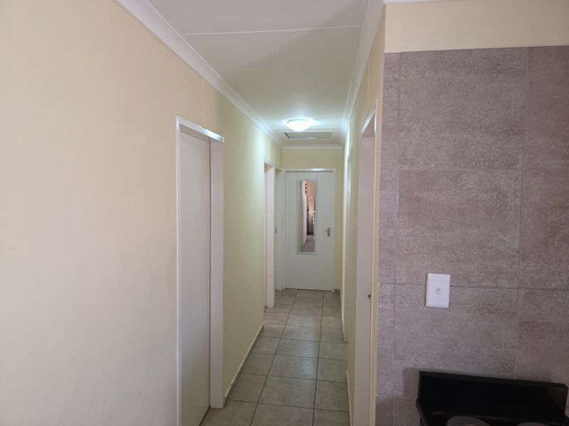 A clean, functional hallway featuring tiled flooring, neutral wall finishes, and multiple internal door access points.