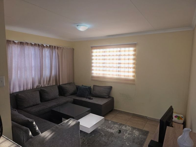 A functional living room featuring tiled flooring, neutral wall finishes, and window blinds, providing a comfortable space for relaxation.