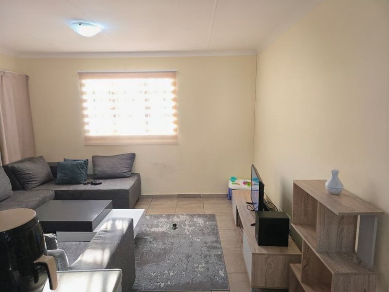 A functional living room featuring tiled flooring, neutral wall finishes, and a window fitted with roller blinds.