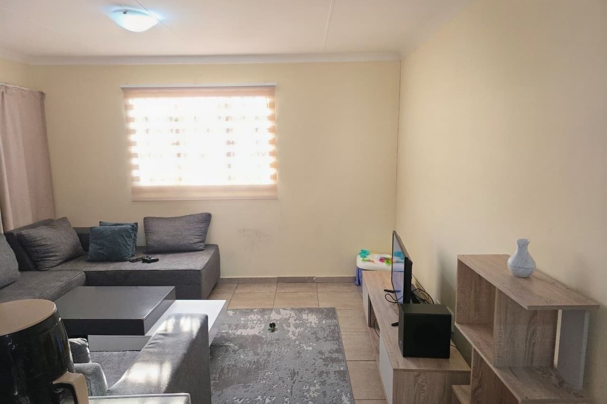 A functional living room featuring tiled flooring, neutral wall finishes, and a window fitted with roller blinds.