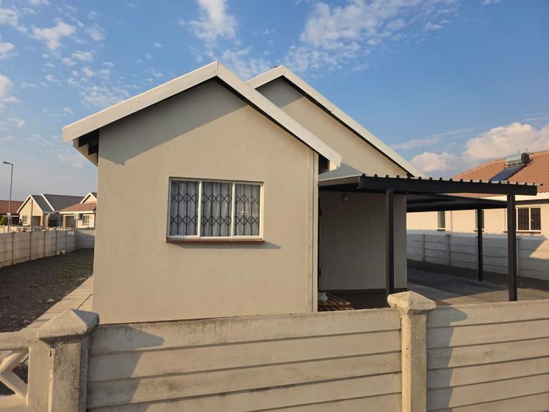 Front view of a residential house featuring a carport, secure window grilles, and a perimeter precast concrete wall.