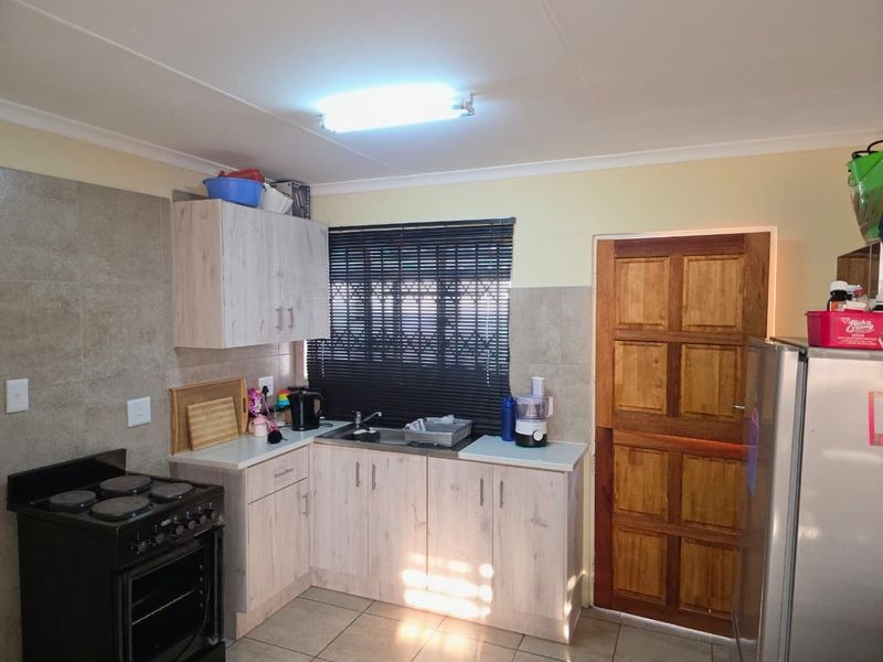 A functional kitchen featuring light wood-look cabinetry, tiled splashbacks, tiled flooring, and a freestanding stove, with direct access to an exterior timber door.
