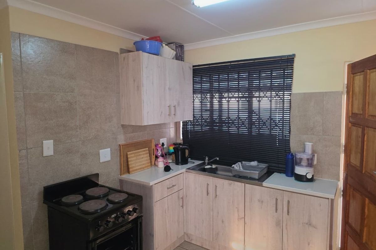 A functional kitchen featuring light wood-look cabinetry, tiled backsplash, stainless steel sink, and a freestanding stove with oven.
