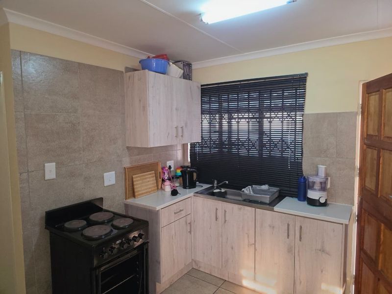 A functional kitchen featuring light wood-look cabinetry, tiled backsplash, stainless steel sink, and a freestanding stove with oven.