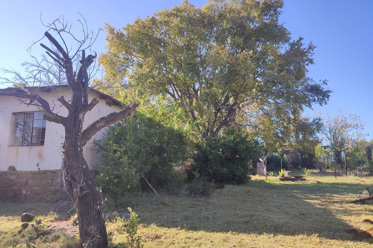 A view of the rear exterior of the farm dwelling, featuring stone foundations, mature trees, and a large garden area.