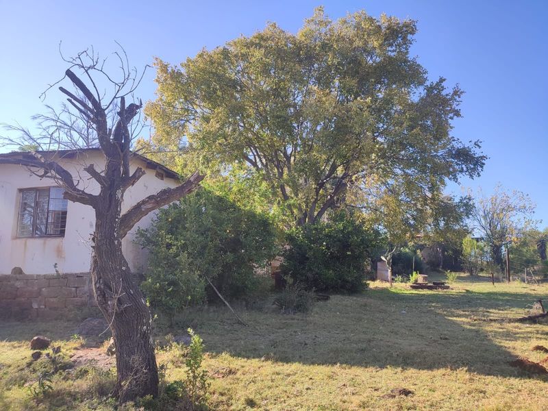 A view of the rear exterior of the farm dwelling, featuring stone foundations, mature trees, and a large garden area.