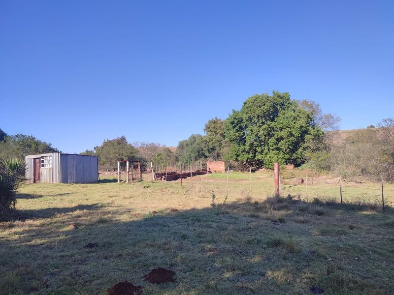 Expansive farm land featuring a corrugated metal storage shed, wire perimeter fencing, and mature trees set against a rural landscape.