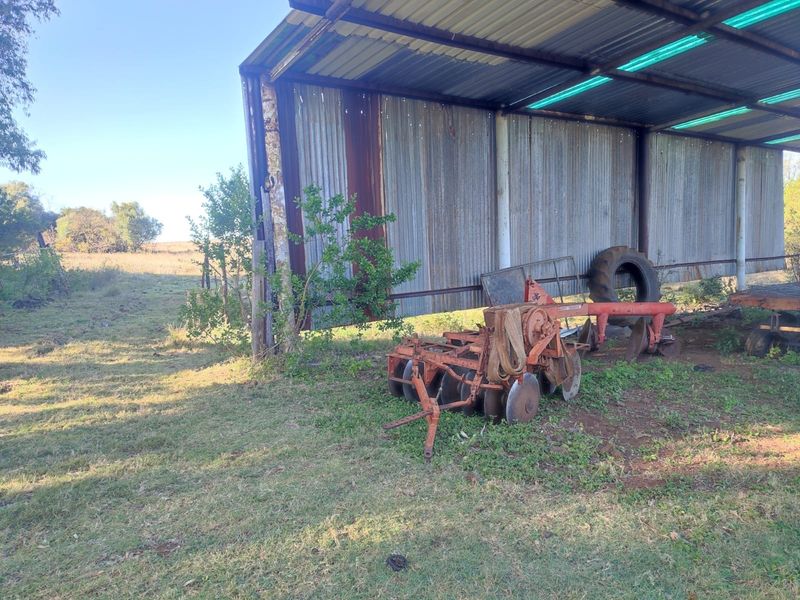 An open-sided agricultural storage shed featuring corrugated metal roofing and siding, suitable for farm equipment storage.