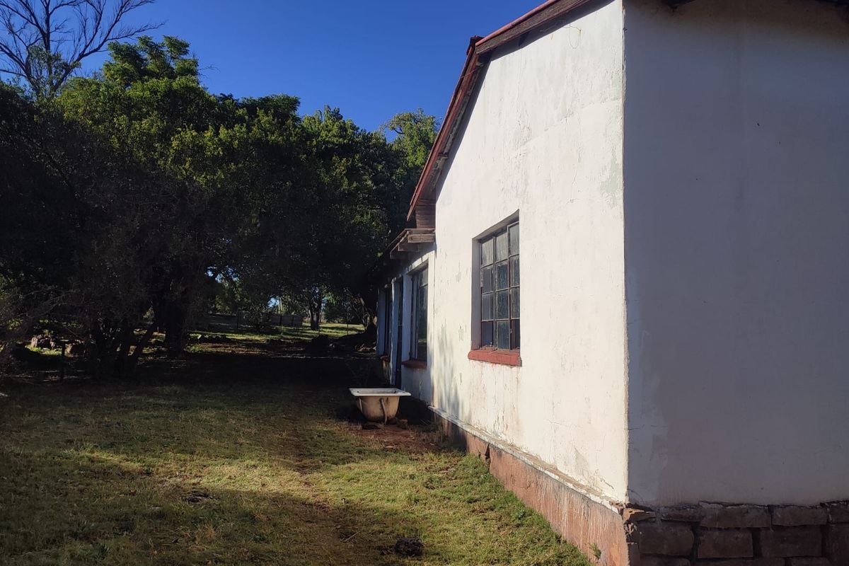 Rear exterior view of a farm building featuring a stone foundation, metal-framed windows, and a corrugated roof, set against a rural landscape.