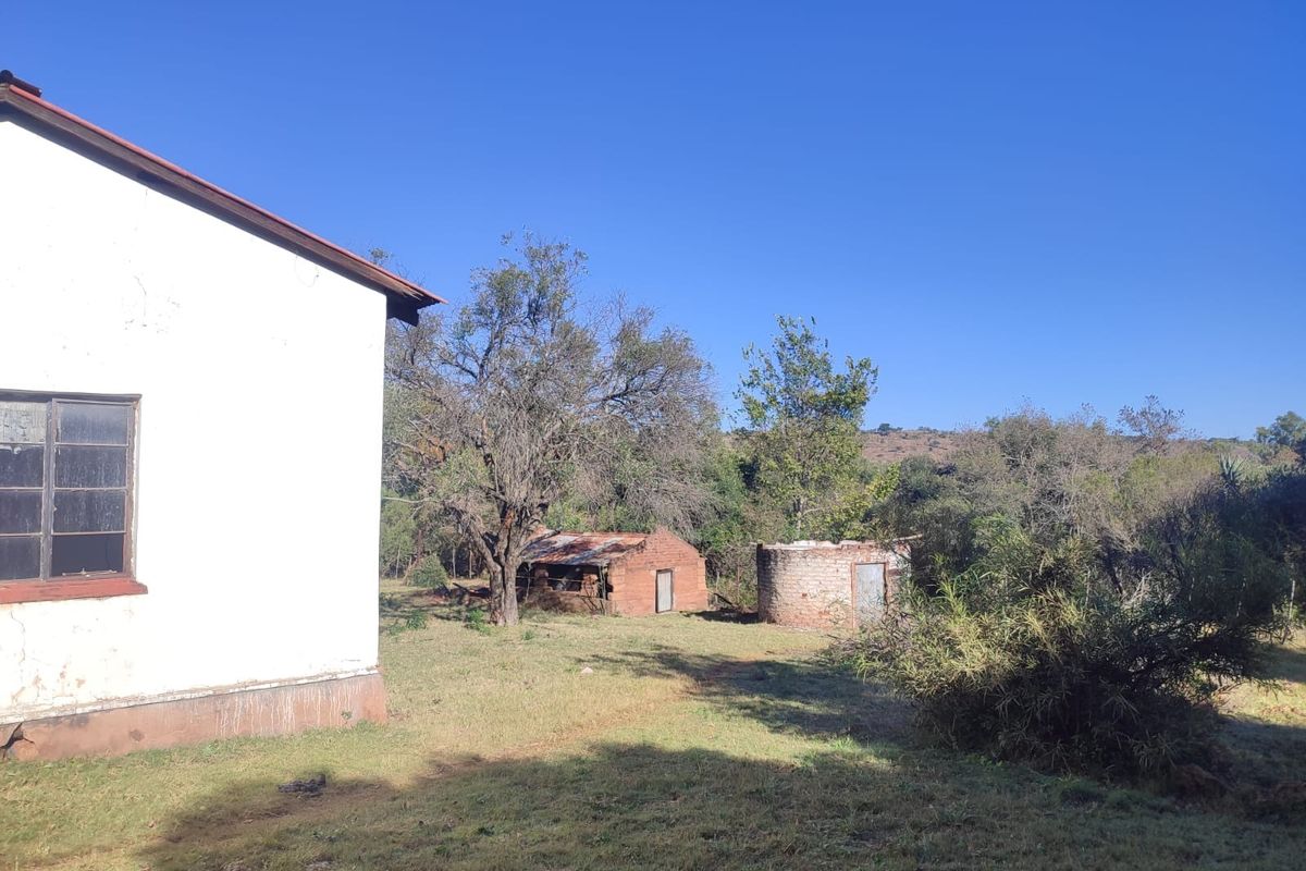 Rear view of the farm property showing the main building exterior, a small brick outbuilding, and a circular structure set within a rural landscape.