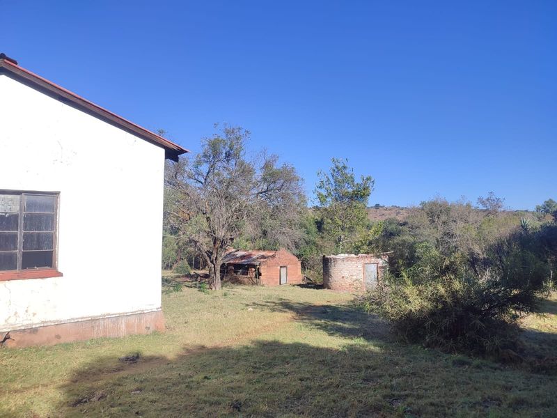 Rear view of the farm property showing the main building exterior, a small brick outbuilding, and a circular structure set within a rural landscape.