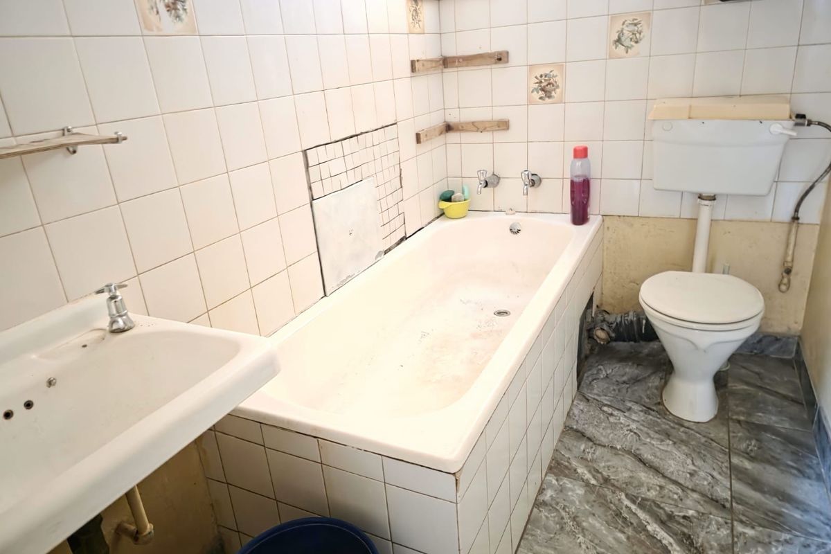 A dated bathroom featuring a standard bathtub, pedestal sink, and toilet, requiring renovation to update the finishes and address visible wear.