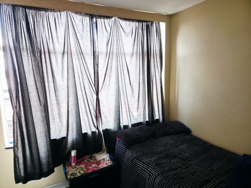 A bedroom featuring a large window with full-length curtains and neutral wall finishes, requiring minor cosmetic updates to the ceiling trim.