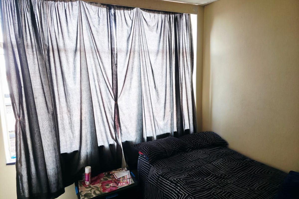 A bedroom featuring a large window with full-length curtains and neutral wall finishes, requiring minor cosmetic updates to the ceiling trim.