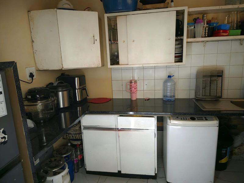 A compact kitchen area featuring laminate countertops, tiled backsplash, and built-in cabinetry, showing signs of wear and requiring cosmetic updates.