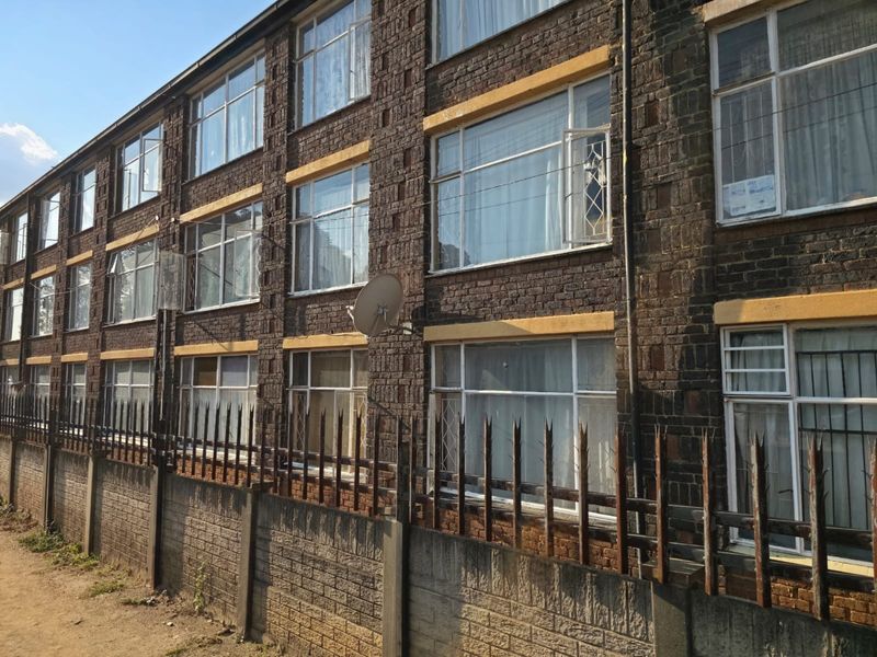 Exterior view of a multi-story brick apartment building featuring metal security fencing and multiple window units.