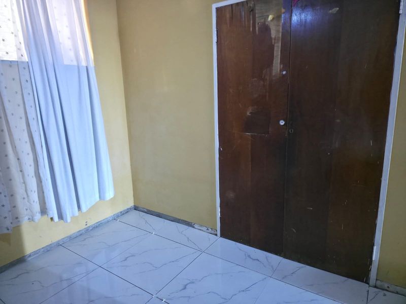 A vacant bedroom featuring tiled flooring and a built-in wooden wardrobe, requiring minor cosmetic updates to the walls and finishes.