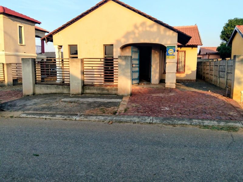Front elevation of a single-story house featuring a tiled roof, paved driveway, and perimeter wall with security gate and bars.