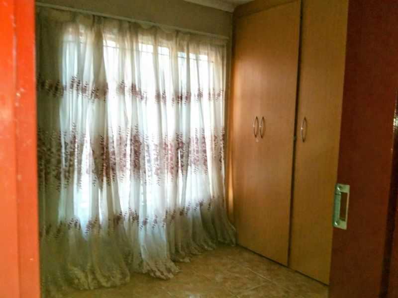 A bedroom featuring built-in wooden cupboards, tiled flooring, and large windows with security bars.