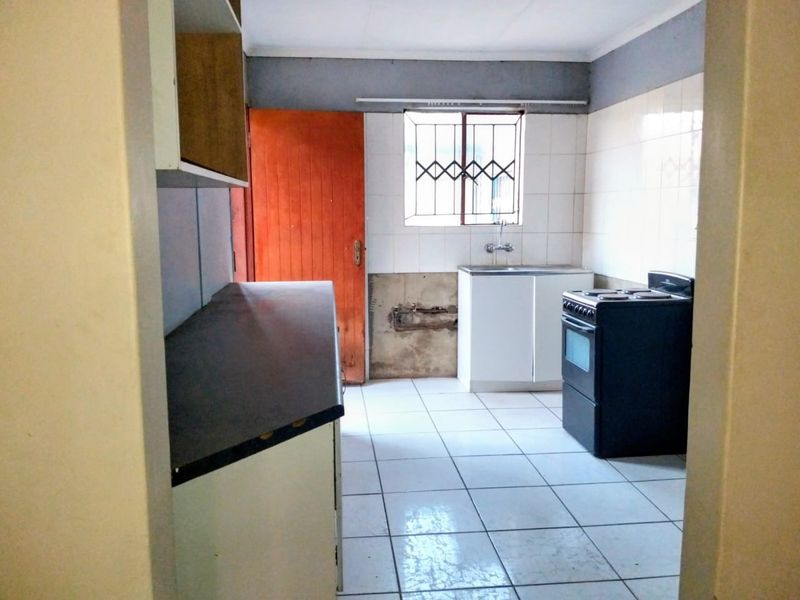 A functional kitchen featuring tiled flooring, a sink, and a freestanding stove, currently requiring cosmetic updates and wall repairs.