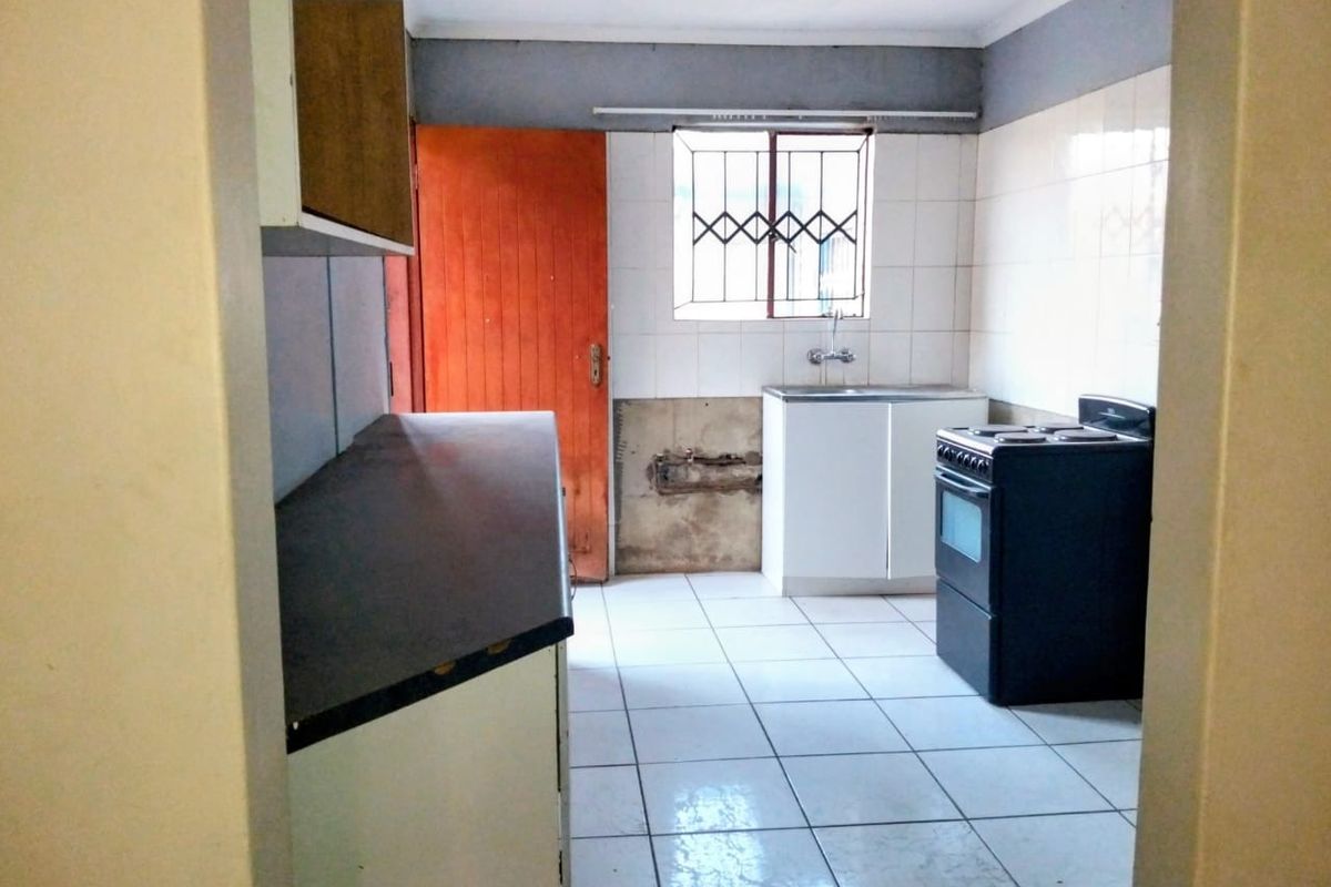 A functional kitchen featuring tiled flooring, a sink, and a freestanding stove, currently requiring cosmetic updates and wall repairs.