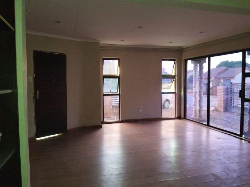 An empty living room featuring laminate flooring, recessed lighting, and large sliding glass doors providing natural light and access to the exterior.