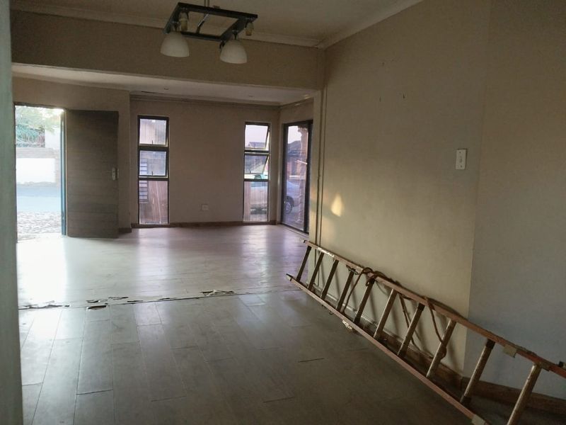 An empty, open-plan living area featuring tiled flooring, aluminium window frames, and a sliding door leading to the exterior.