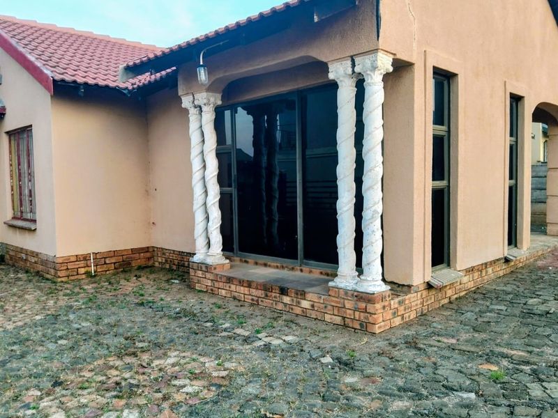 A covered patio area featuring decorative columns and sliding glass doors, with visible wear to the exterior plaster and paving.
