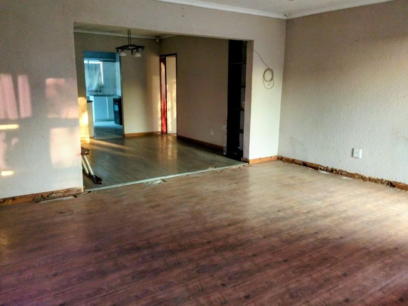 An empty open-plan living area featuring laminate flooring, visible skirting board damage, and exposed wiring, offering a blank canvas for renovation.