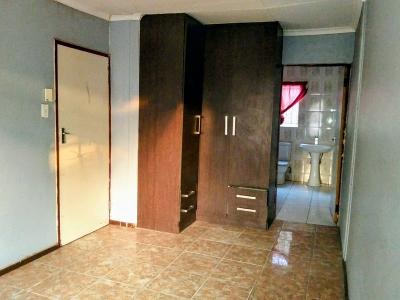 A vacant bedroom featuring tiled flooring, a built-in wardrobe, and direct access to an en-suite bathroom.