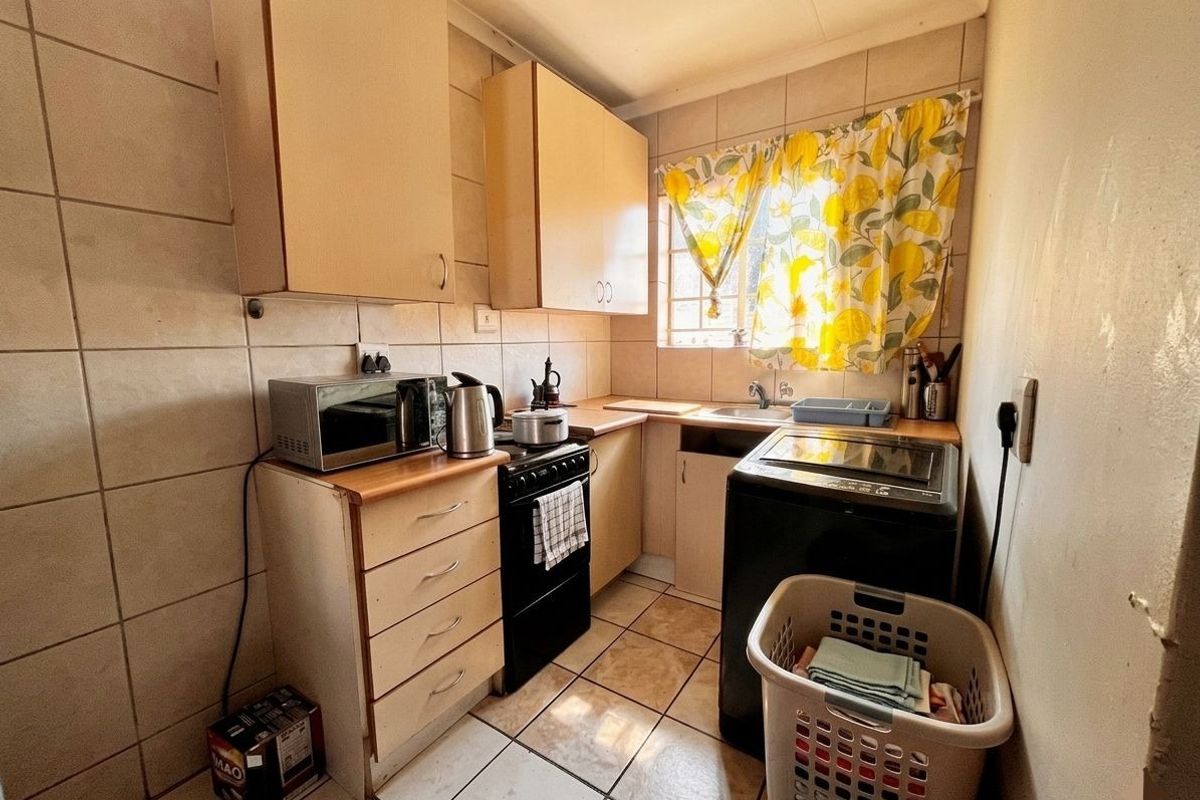 A compact kitchen featuring tiled walls and flooring, built-in cabinetry, a stainless steel sink, and a freestanding stove.