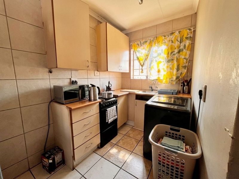 A compact kitchen featuring tiled walls and flooring, built-in cabinetry, a stainless steel sink, and a freestanding stove.