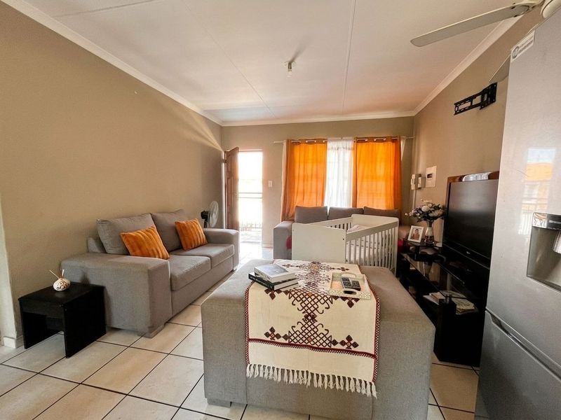 A functional living room featuring tiled flooring, a ceiling fan, and direct access to an exterior area through a doorway.