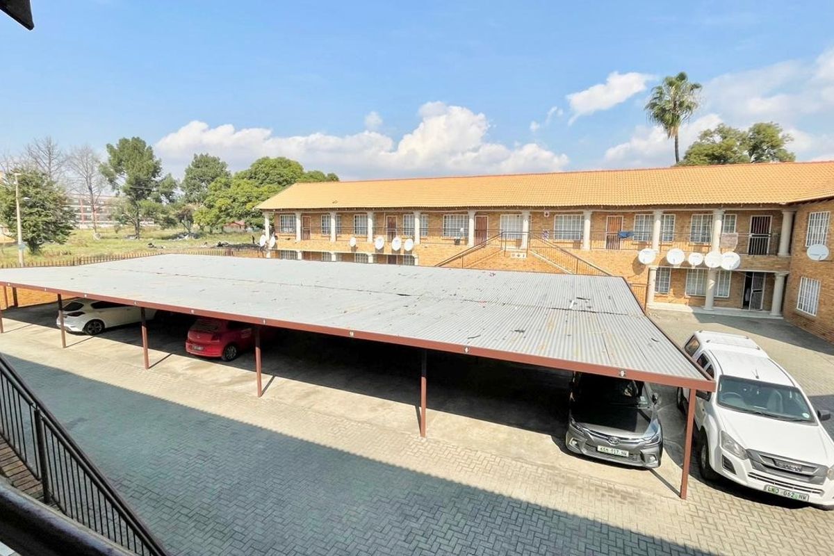 Exterior view of an apartment complex featuring a large covered carport area with paved driveway and brick building facade.