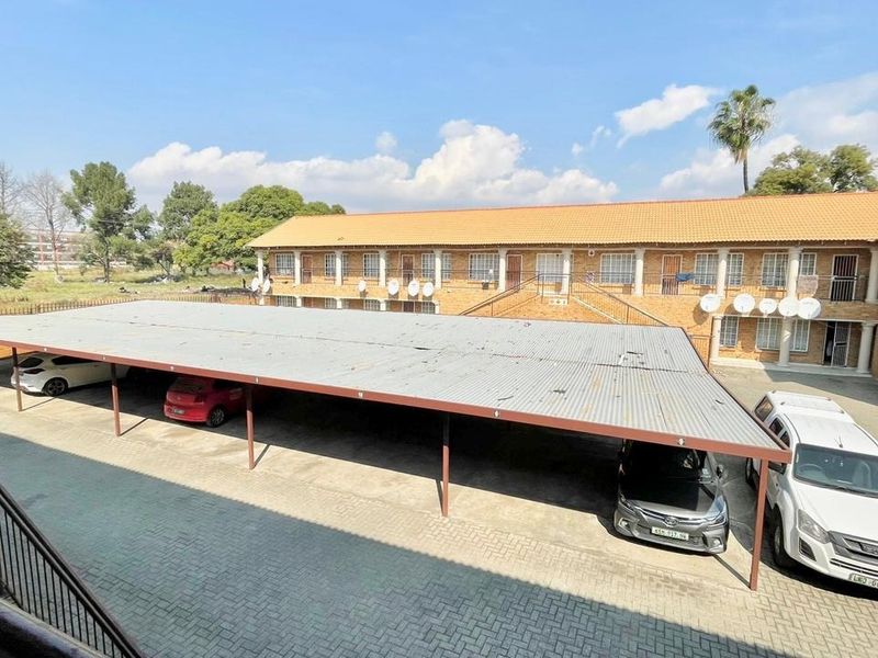 Exterior view of an apartment complex featuring a large covered carport area with paved driveway and brick building facade.