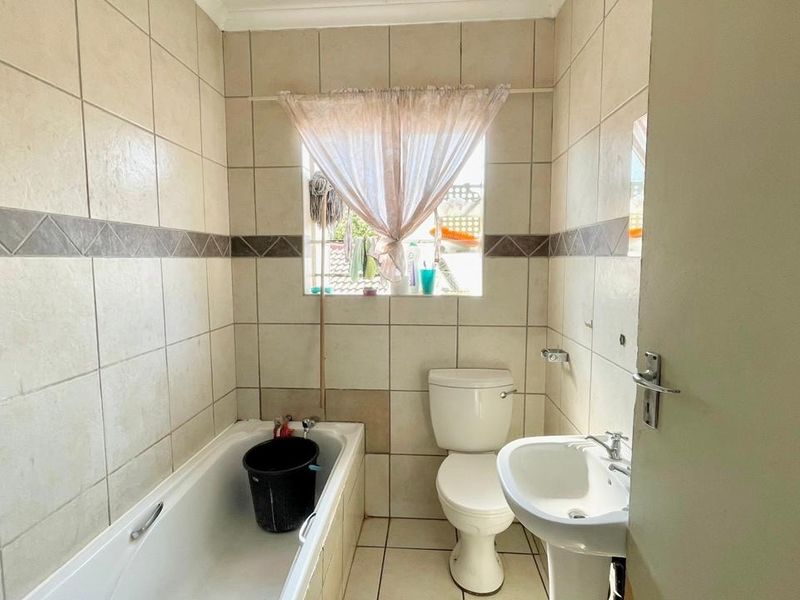 A functional bathroom featuring a bathtub, pedestal basin, and toilet with neutral wall and floor tiling.