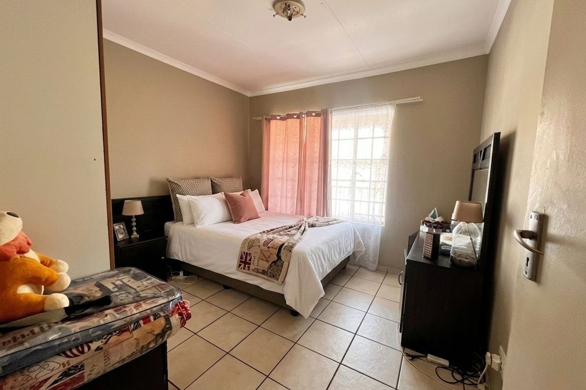 A functional bedroom featuring tiled flooring, a coved ceiling, and a window fitted with security bars.