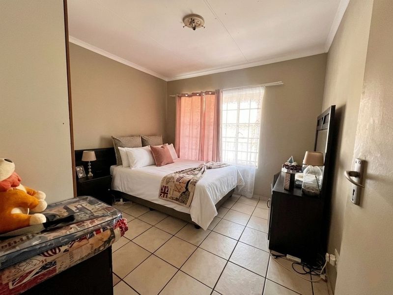 A functional bedroom featuring tiled flooring, a coved ceiling, and a window fitted with security bars.